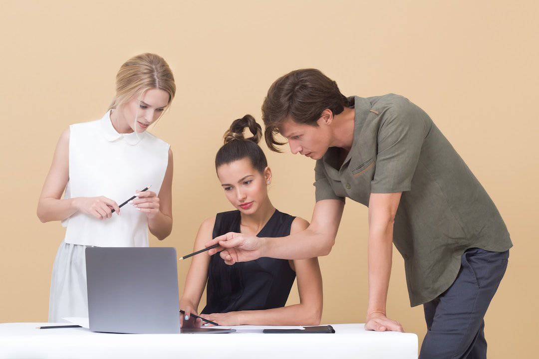 A few different employees studying a laptop while one guy points at the screen with his pen.